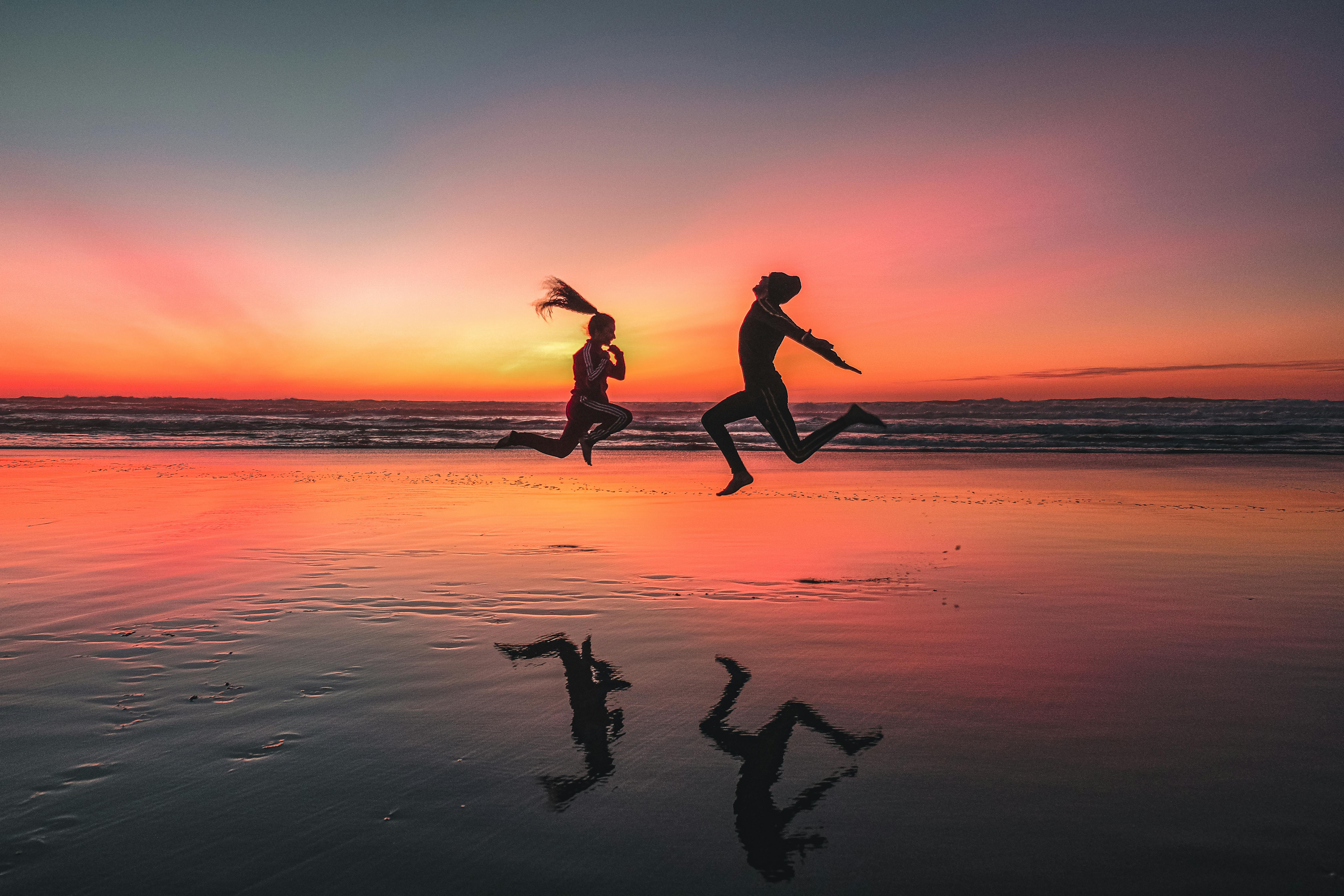 Two people jumping for joy on the beach at sunset
