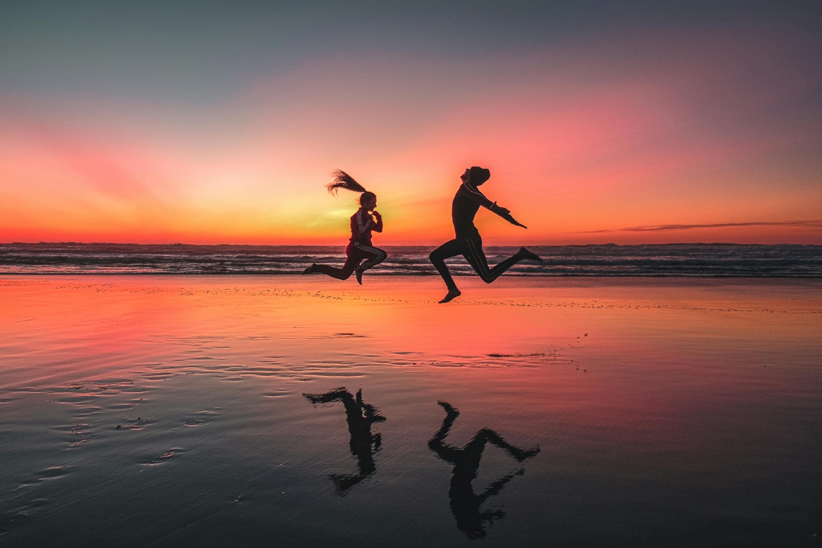 Two people jumping for joy on the beach at sunset